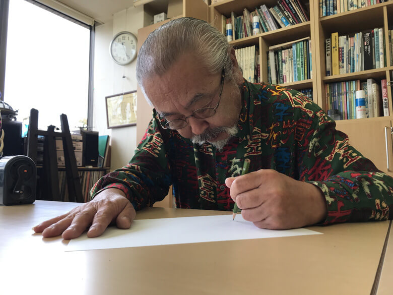 アトリエで魚を描く小村氏。その様子は、BuNaの記事でご覧いただけます。
