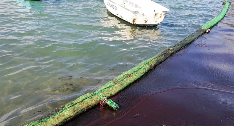 事故直後、流出した重油の拡散を食い止めるため、現場近くの沿岸に敷設されたオイルフェンス。フェンスの右側まで黒い重油が迫っています。