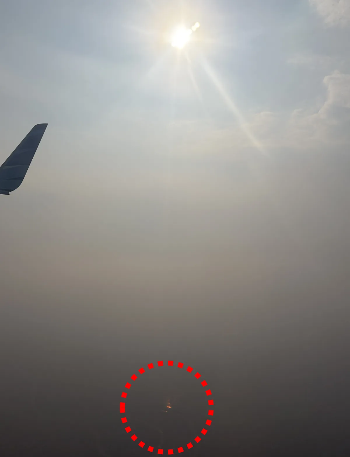帰りの飛行機から撮った写真。太陽は白く見えていますが、水田に反射した太陽(赤で囲った部分)は、不気味な赤い色をしています。